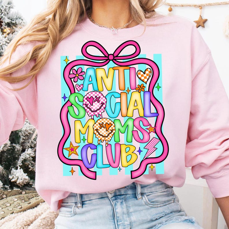 K&ouml;nnte beinhalten: Hellrosa Sweatshirt mit dem Schriftzug "ANTI SOCIAL MOMS CLUB" in einem farbenfrohen, cartoonartigen Design. Das Design umfasst Blumen, Sterne und Blitze. Das Sweatshirt hat lange &Auml;rmel und einen Rundhalsausschnitt.