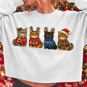 K&ouml;nnte beinhalten: Ein wei&szlig;es Langarm-Sweatshirt mit einem Grafikdruck von vier Katzen in festlicher Kleidung. Die Katzen tragen Pullover, Schals und Stirnb&auml;nder mit Rentiergeweihen oder Weihnachtsm&uuml;tzen sowie jeweils eine runde Brille.