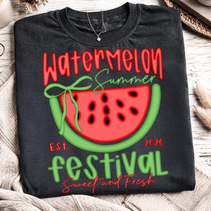 以下が含まれることがあります： スイカのスライスグラフィックが特徴の濃い灰色のTシャツ。「Watermelon Summer Festival Sweet and Fresh」の文字が赤と緑でデザインされており、2026年と書かれています。