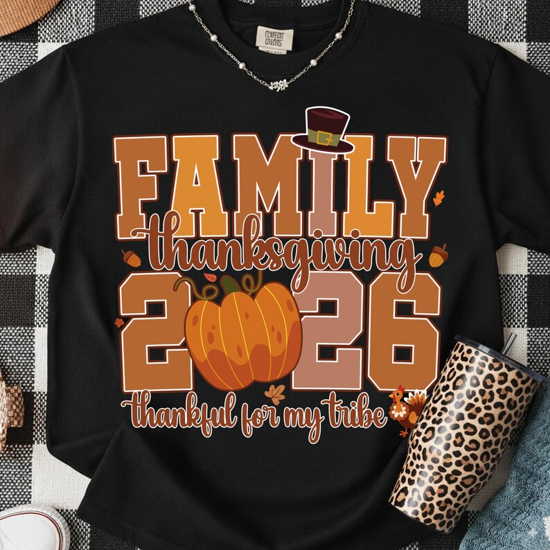 Pode incluir: Uma t-shirt preta de manga curta com uma estampa gr&aacute;fica contendo o texto FAMILY THANKSGIVING 2026 e thankful for my tribe. O design inclui uma ab&oacute;bora laranja grande, um chap&eacute;u de peregrino castanho, bolotas e um peru em tons de outono.