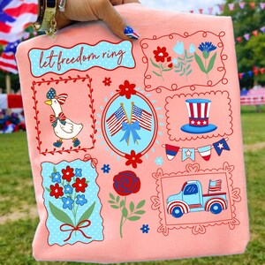 May include: A peach-colored t-shirt featuring patriotic illustrations. Designs include a goose, flowers, flags, and a truck, all framed with red borders. The text "let freedom ring" is also displayed.
