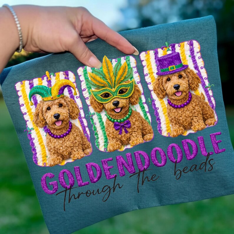 May include: Teal fabric featuring three embroidered Goldendoodles in Mardi Gras attire. Each dog wears a different festive accessory: a jester hat, a mask, and a top hat. The text "GOLDENDOODLE Through The beads" is embroidered below the dogs.