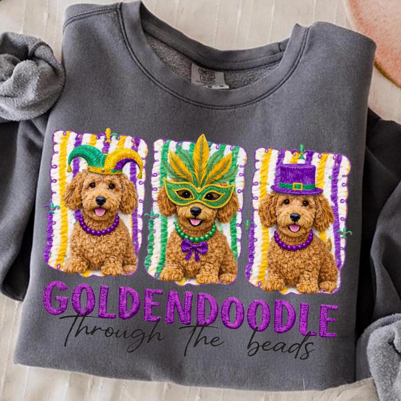 May include: Dark gray sweatshirt featuring three Golden Doodle dogs in Mardi Gras attire. Each dog wears a different hat or mask, with purple and green beaded necklaces. The text "GOLDENDOODLE Through The beads" is embroidered below.