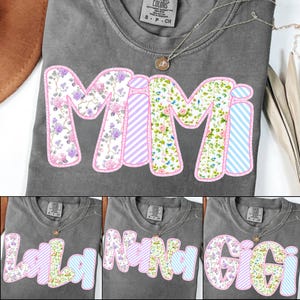 May include: A gray t-shirt with the word "Mimi" in a floral and striped design. The letters are outlined in pink. A necklace with a small pendant is visible. Additional shirts with different names are shown below.