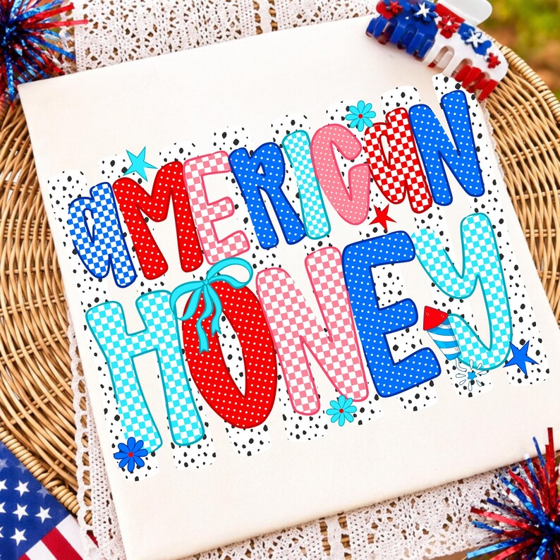 May include: A white t-shirt featuring the text AMERICAN HONEY in a multi-colored, patterned font. The letters are decorated with red, blue, and pink polka dots and checkerboard patterns, accented with small stars, flowers, and a firework graphic.