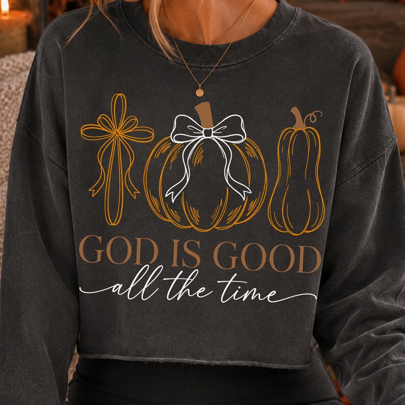 Puede incluir: Una sudadera gris carb&oacute;n de manga larga con un estampado gr&aacute;fico de una cruz, una calabaza con un lazo blanco y una calabaza alargada. El texto dice GOD IS GOOD en letras marrones y all the time en letra cursiva blanca debajo de los gr&aacute;ficos.