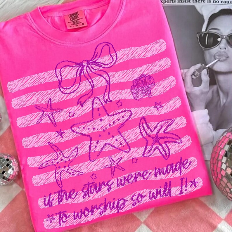 Op de afbeelding: Felroze Comfort Colors T-shirt met een paars zeester- en strikdesign. Het shirt heeft de tekst "if the stars were made to worship so will I!" en horizontale strepen.