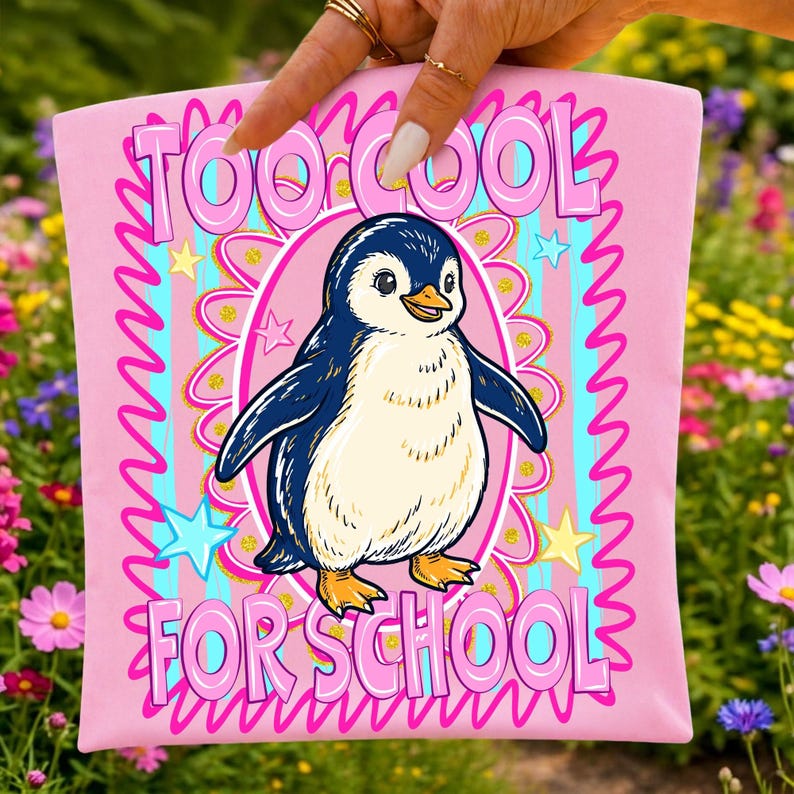 K&ouml;nnte beinhalten: Rosafarbenes T-Shirt mit einer Cartoon-Pinguin-Illustration. Der Pinguin ist blau, wei&szlig; und gelb und befindet sich in einem rosa Oval. Der Text "TOO COOL FOR SCHOOL" ist rosa, wei&szlig; umrandet und umgibt den Pinguin.