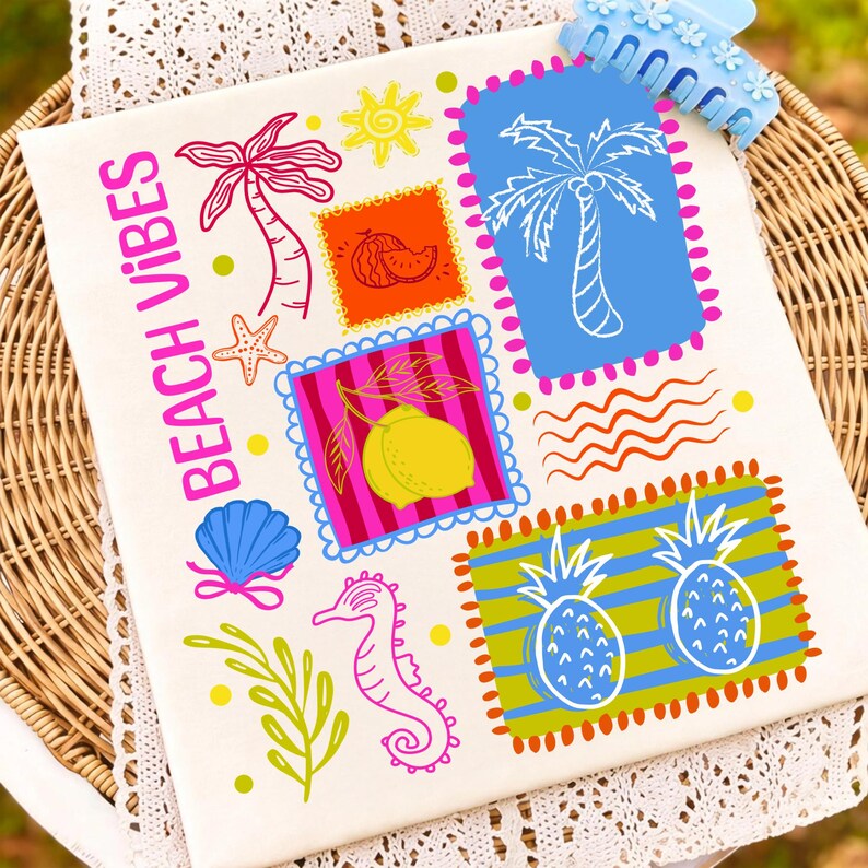 May include: A white canvas tote bag featuring vibrant beach-themed designs, such as palm trees, a seashell, and pineapples. The words "BEACH VIBES" are printed in pink. A blue hair clip is placed on the top right corner.