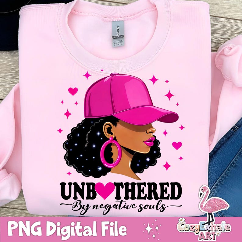 May include: Pink sweatshirt featuring a graphic of a Black woman wearing a pink baseball cap and a large pink heart with the text "Unbothered by negative souls".