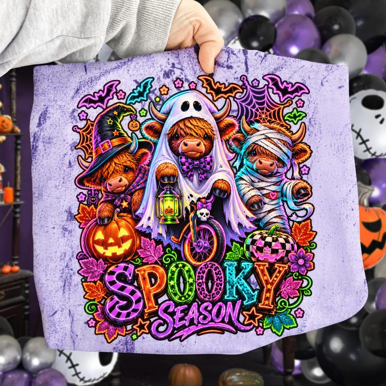 Może przedstawiać: Jasnofioletowy materiał z grafiką trzech kr&oacute;w rasy Highland przebranych na Halloween: czarownica z dynią, duch na rowerze z latarnią oraz mumia. Napis Spooky Season wykonany jest kolorowymi literami na środku nadruku.