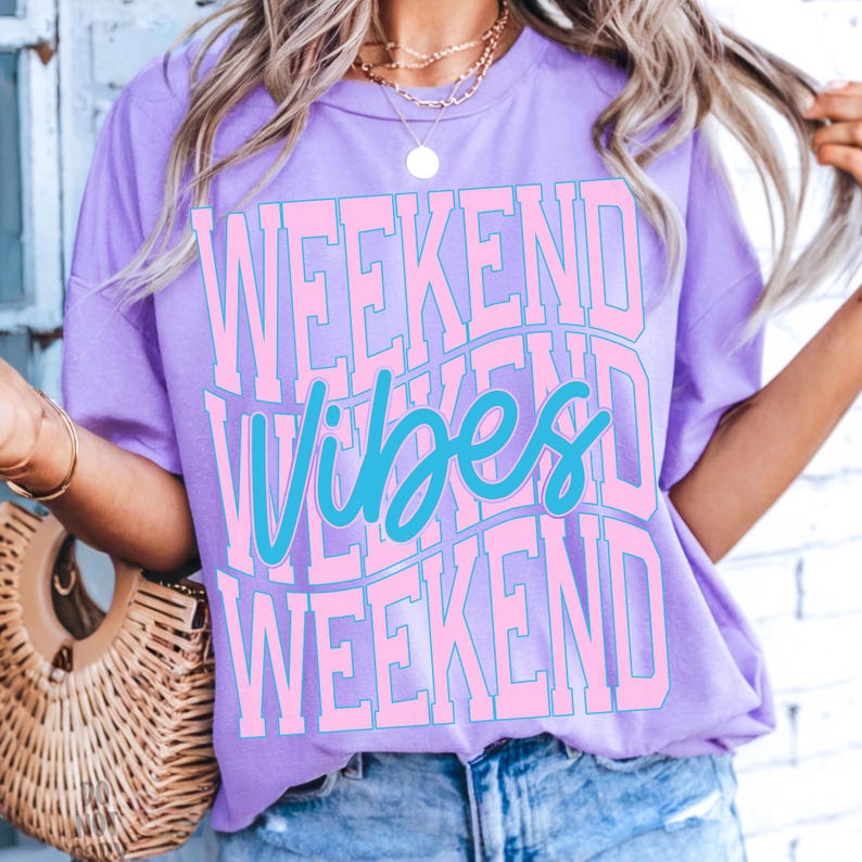 K&ouml;nnte beinhalten: Ein lilafarbenes T-Shirt mit dem Schriftzug "WEEKEND VIBES WEEKEND" in einem wellenf&ouml;rmigen Design. Der Text ist hellrosa mit dem Wort "Vibes" in t&uuml;rkisfarbener Schrift. Das Shirt hat einen Rundhalsausschnitt und kurze &Auml;rmel.