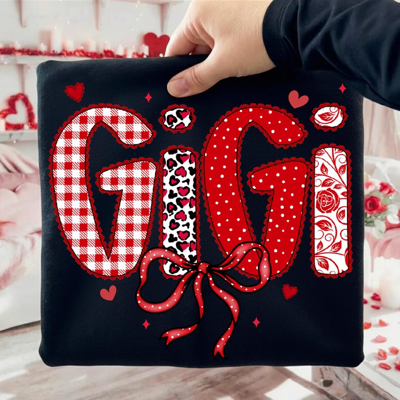 Może przedstawiać: Czarna bluza z napisem "GIGI" w patchworkowym wzorze. Litery mają czerwono-białą kratę, czerwone kropki i wz&oacute;r w cętki. Czerwona kokarda znajduje się na dole, a małe serca i diamenty są rozrzucone wok&oacute;ł imienia.