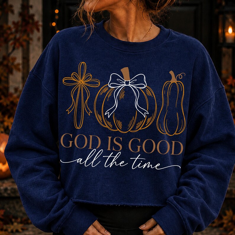 Puede incluir: Una sudadera azul marino de manga larga con un estampado gr&aacute;fico de una cruz, una calabaza con un lazo blanco y una calabaza alargada. El texto "GOD IS GOOD" aparece en negrita sobre el texto en cursiva "all the time" en color blanco.