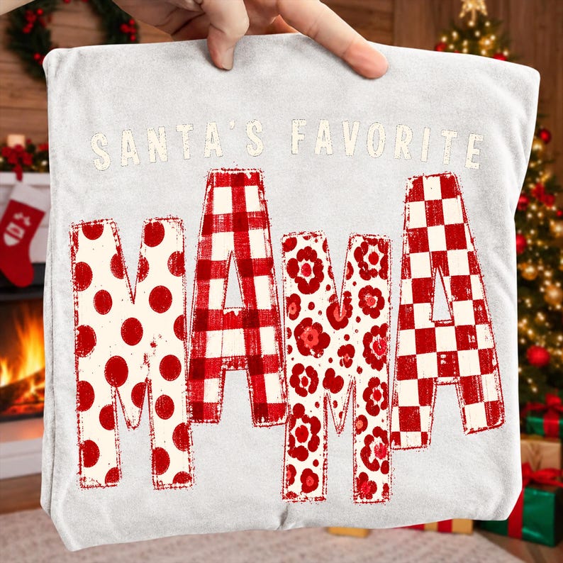 K&ouml;nnte beinhalten: Ein hellgraues T-Shirt mit dem Schriftzug SANTA'S FAVORITE in wei&szlig;en Buchstaben &uuml;ber dem Wort MAMA. Die Buchstaben von MAMA sind mit rot-wei&szlig;en Mustern gef&uuml;llt, darunter Punkte, ein B&uuml;ffelkaromuster, Blumenmotive und ein Schachbrettmuster.