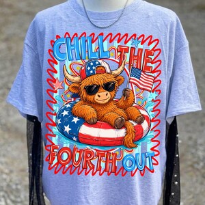 May include: Light blue t-shirt featuring a cartoon Highland cow wearing sunglasses and a patriotic hat, floating in a red, white, and blue inner tube. The shirt has the text "Chill the Fourth Out" in a wavy font.