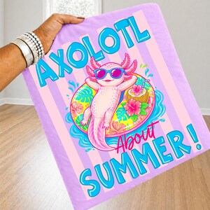 Peut inclure: Une couverture lilas avec un axolotl de dessin anim&eacute; portant des lunettes de soleil et se relaxant sur un flotteur. La couverture porte les mots "AXOLOTL About SUMMER!" en bleu et rose.