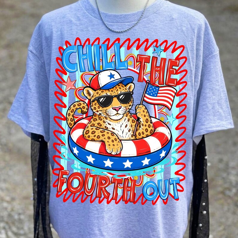 Op de afbeelding: Lichtblauw T-shirt met een afbeelding van een luipaard met een zonnebril en een patriottische hoed, drijvend in een rood, wit en blauw zwemband. De tekst "Chill the Fourth Out" is weergegeven in een golvend lettertype.