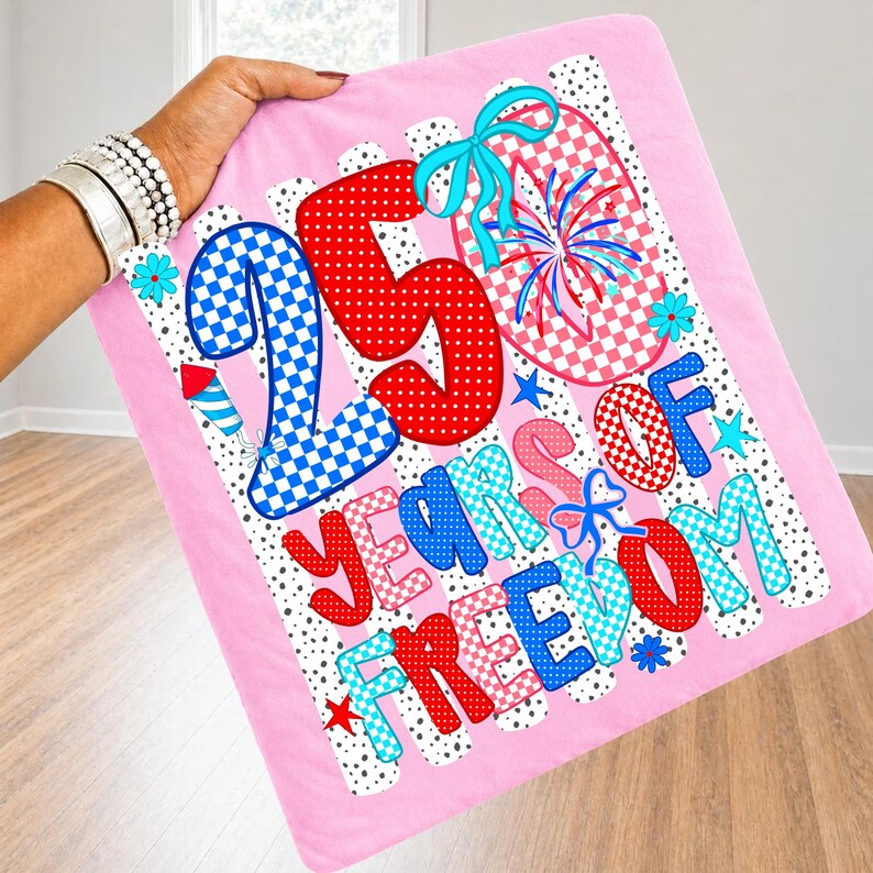 K&ouml;nnte beinhalten: Ein rosa Stoffquadrat mit einem grafischen Design und dem Text 25 YEARS OF FREEDOM. Das Design enth&auml;lt rot-wei&szlig;-blaue Karomuster, Punkte, Feuerwerk, Sterne und hellblaue Schleifen auf einem wei&szlig;en Hintergrund mit schwarzen Punkten.