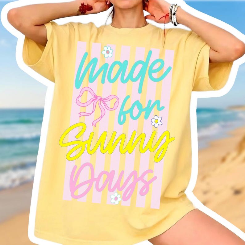 K&ouml;nnte beinhalten: Gelbes T-Shirt mit dem Text "Made for Sunny Days" in T&uuml;rkis, Gelb und Rosa. Das Design beinhaltet eine rosa Schleife und kleine Blumen. Das Shirt hat kurze &Auml;rmel und eine lockere Passform, ideal f&uuml;r den Alltag.