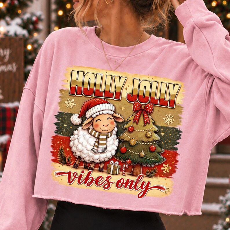 Może przedstawiać: Jasnor&oacute;żowa kr&oacute;tka bluza z nadrukiem owcy w czapce Mikołaja i szaliku obok udekorowanej choinki. Powyżej znajduje się napis HOLLY JOLLY, a poniżej napis vibes only.