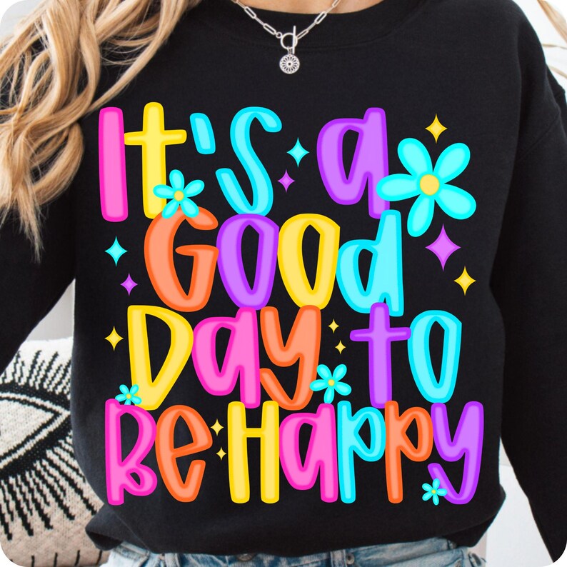 K&ouml;nnte beinhalten: Schwarzer Pullover mit einer bunten Grafik, auf der "It's a good day to be happy" steht. Die Grafik zeigt Blumen und Sterne.