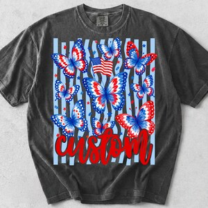 Peut inclure: Un t-shirt gris anthracite avec une impression graphique de plusieurs papillons aux motifs rouges, blancs et bleus. Le design comprend un petit drapeau am&eacute;ricain, des &eacute;toiles &eacute;parpill&eacute;es, des rayures verticales bleu clair et le mot custom en rouge.