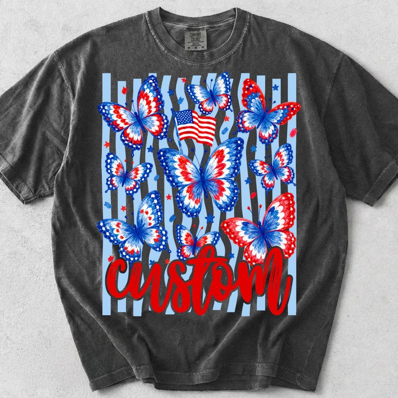 Peut inclure: Un t-shirt gris anthracite avec une impression graphique de plusieurs papillons aux motifs rouges, blancs et bleus. Le design comprend un petit drapeau am&eacute;ricain, des &eacute;toiles &eacute;parpill&eacute;es, des rayures verticales bleu clair et le mot custom en rouge.