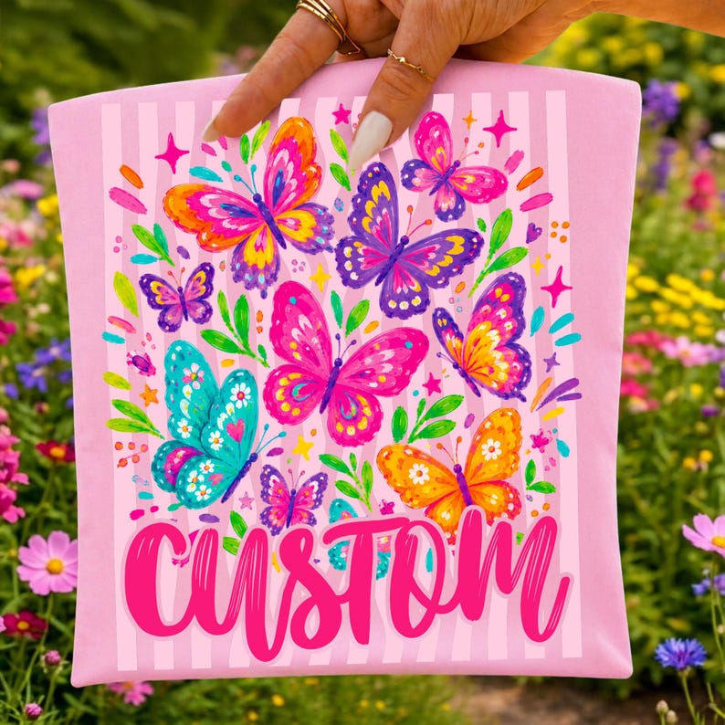 May include: A light pink fabric pouch featuring a vertical striped pattern and a colourful graphic print of various butterflies in shades of orange, purple, pink, and teal, with the word CUSTOM written in large, bold, bright pink script at the bottom.