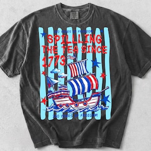 Pu&ograve; includere: T-shirt grigio scuro con un design grafico raffigurante una nave rossa, bianca e blu che naviga sulle onde. Il testo "Spilling the Tea Since 1773" &egrave; in rosso, con strisce verticali blu e stelle. La maglietta ha anche il testo "250 Years of Freedom".