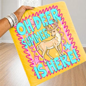 K&ouml;nnte beinhalten: Gelbe Decke mit dem Text "OH DEER SUMMER IS HERE!" in t&uuml;rkisfarbenen Buchstaben. In der Mitte befindet sich ein Cartoon-Hirsch. Die Decke hat einen rosa und gelben Wellenrand und rosa Sterne.