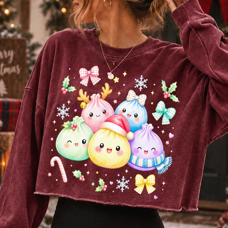 May include: A maroon long-sleeve sweatshirt featuring a graphic print of five colourful, smiling dumpling characters. The dumplings are decorated with a Santa hat, a scarf, and reindeer antlers, surrounded by snowflakes, bows, and holly berries.