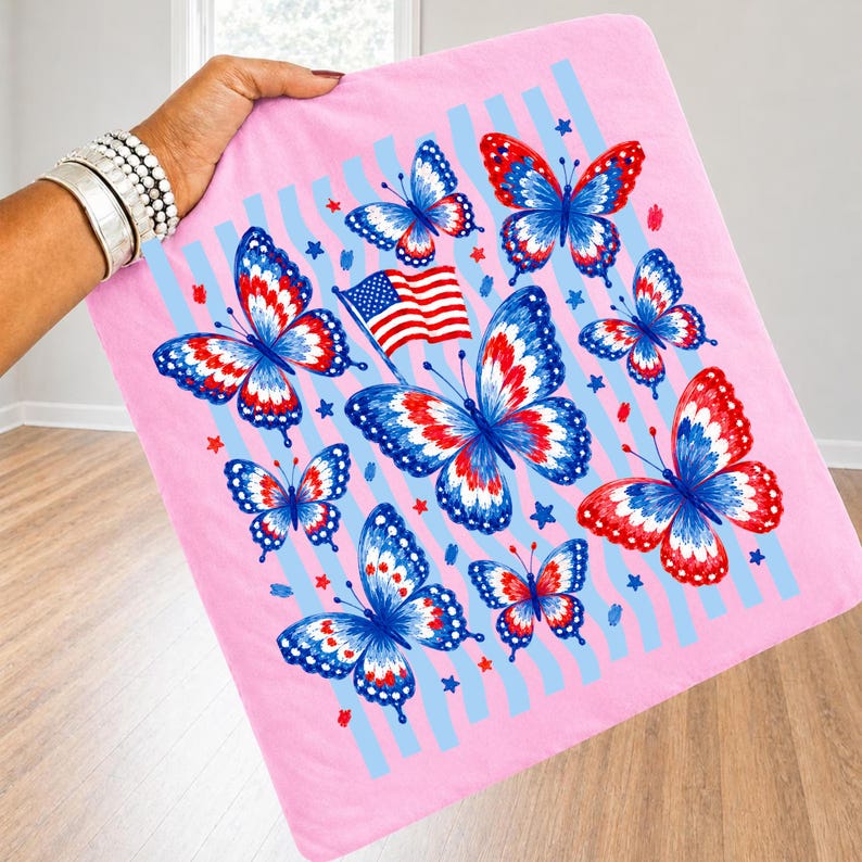 Puede incluir: Un art&iacute;culo de tela cuadrado con un patr&oacute;n de mariposas en colores rojo, blanco y azul. El dise&ntilde;o incluye una peque&ntilde;a bandera estadounidense y estrellas azules y rojas dispersas sobre rayas verticales de color azul claro en rosa.