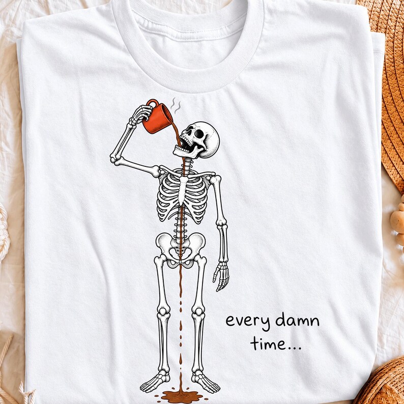 May include: A white t-shirt featuring a graphic of a skeleton drinking from a red mug, with coffee pouring through its ribcage and onto the floor. The text "every damn time..." is printed in black lettering to the right of the skeleton's legs.