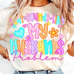 K&ouml;nnte beinhalten: Cremefarbenes T-Shirt mit dem Schriftzug "Sounds Like My Husbands Problem" in bunten Buchstaben. Das Design umfasst Herzen und Blumen in Rosa, Blau, Orange und Gelb.