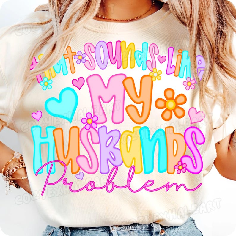 K&ouml;nnte beinhalten: Cremefarbenes T-Shirt mit dem Schriftzug "Sounds Like My Husbands Problem" in bunten Buchstaben. Das Design umfasst Herzen und Blumen in Rosa, Blau, Orange und Gelb.