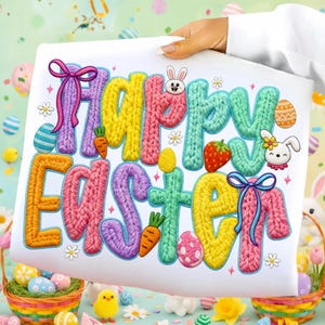 May include: A white fabric with the words "Happy Easter" in colorful, knitted-style letters. The design includes Easter eggs, carrots, strawberries, and bunny illustrations, with bows and floral accents. The image is held by a person.