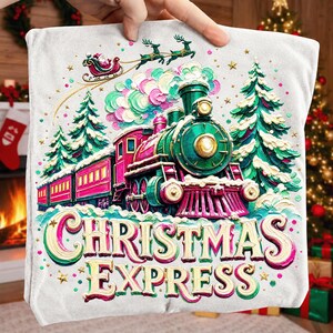 May include: A light grey t-shirt featuring a colourful graphic of a steam train, evergreen trees, and Santa in a sleigh. The train is green and magenta with gold accents. The text CHRISTMAS EXPRESS is printed in large, stylised gold and magenta letters.