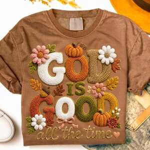 Pu&ograve; includere: Una t-shirt marrone a maniche corte con un disegno ricamato che riporta la scritta "GOD IS GOOD all the time". La grafica include zucche colorate, foglie autunnali e vari fiori nelle tonalit&agrave; del bianco, rosa, arancione e verde.