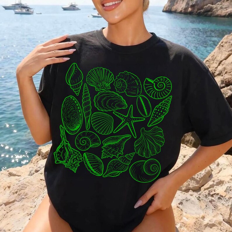 K&ouml;nnte beinhalten: Schwarzes T-Shirt mit einem neongr&uuml;nen Muscheldesign. Das Design umfasst verschiedene Muschelillustrationen, wie z. B. Muschelschalen, Jakobsmuscheln und einen Seestern. Das Shirt ist ein l&auml;ssiger, bequemer Stil.