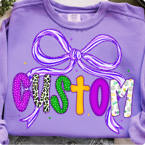 May include: A purple sweatshirt with the word "CUSTOM" in colorful letters. The "C" is polka-dotted, the "U" has a leopard print, the "S" is green with polka dots, the "T" is yellow, the "O" is purple, and the "M" has a floral pattern. A purple bow is above the word.