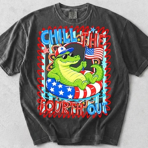 K&ouml;nnte beinhalten: Dunkelgraues T-Shirt mit einem Cartoon-Alligator, der eine Sonnenbrille und einen patriotischen Hut tr&auml;gt und sich auf einem rot-wei&szlig;-blauen Schwimmreifen entspannt. Das Shirt tr&auml;gt die Worte "Chill the Fourth Out" in einem farbenfrohen Design.