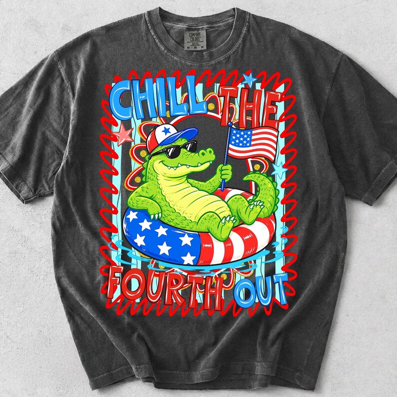 K&ouml;nnte beinhalten: Dunkelgraues T-Shirt mit einem Cartoon-Alligator, der eine Sonnenbrille und einen patriotischen Hut tr&auml;gt und sich auf einem rot-wei&szlig;-blauen Schwimmreifen entspannt. Das Shirt tr&auml;gt die Worte "Chill the Fourth Out" in einem farbenfrohen Design.