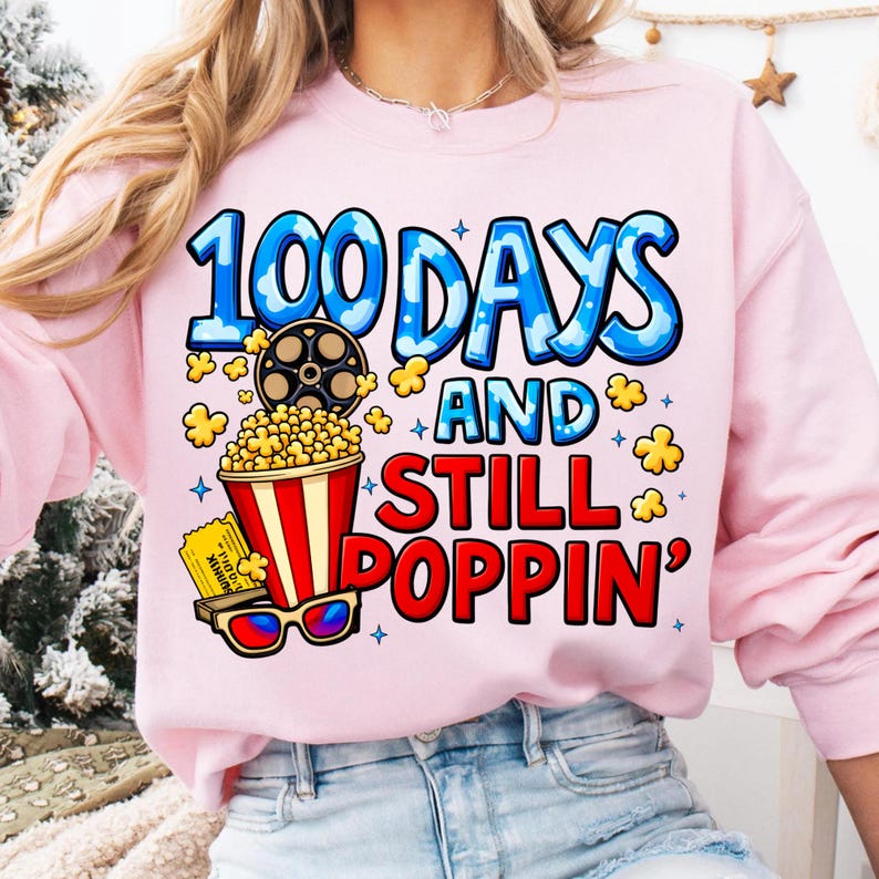 Puede incluir: Sudadera rosa claro con el texto "100 DAYS AND STILL POPPIN'" en azul y rojo. El dise&ntilde;o incluye una bobina de pel&iacute;cula, palomitas de ma&iacute;z, una entrada de cine y gafas 3D. Un estilo casual y c&oacute;modo.