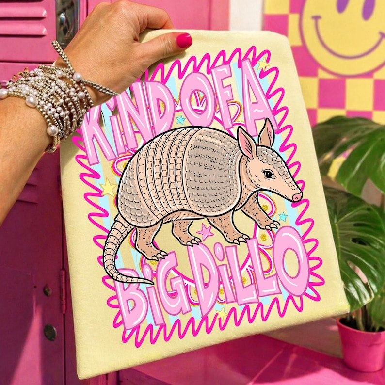 May include: A light yellow armadillo-themed graphic art print with the text "KIND OF A BIG DILLO" in pink. The armadillo is tan and pink, with a detailed shell. The background has blue and yellow accents.