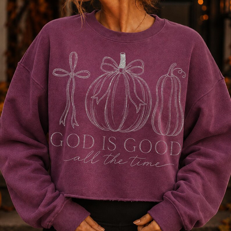 K&ouml;nnte beinhalten: Ein pflaumenfarbenes Langarm-Sweatshirt mit einer wei&szlig;en Strichgrafik, die ein Kreuz mit Schleife, einen K&uuml;rbis mit Schleife und einen Flaschenk&uuml;rbis zeigt. Der Text "GOD IS GOOD all the time" ist in Wei&szlig; unter den Illustrationen aufgedruckt.
