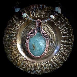 May include: A copper wire wrapped pendant featuring a light blue oval gemstone. The pendant is on a silver chain with beads.