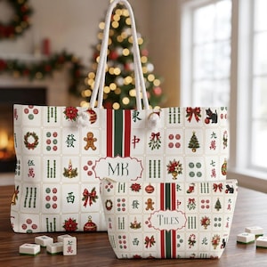 May include: A white tote bag and a matching zippered pouch featuring a repeating pattern of mahjong tiles decorated with Christmas motifs like gingerbread men, wreaths, and trees. The tote displays the initials MK, while the pouch says TILES.