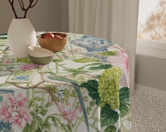 Puede incluir: Un mantel redondo con un diseño floral y de pájaros. El mantel presenta flores rosas, hojas verdes y un patrón de enrejado. Un jarrón blanco, un cuenco pequeño y una cesta de manzanas están sobre la mesa.