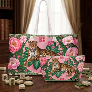 May include: A large tote bag and a smaller matching pouch featuring a leopard resting on green leaves within a pink circular frame, surrounded by pink peony flowers on a green background with white rope handles and a geometric border pattern.